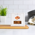Jocelyn & Co. Candied Pecans Box, upright on a wooden board in a softly lit kitchen setting