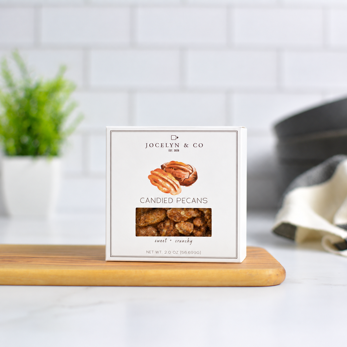 Jocelyn & Co. Candied Pecans Box, upright on a wooden board in a softly lit kitchen setting