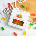 Jocelyn & Co. Mixed Gummi Bears 3 oz square box with watercolor bear artwork and a clear candy window, styled with loose gummi bears on a bamboo board and pale countertop
