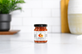 Jocelyn & Co. Sweet Peach & Bourbon Jam in an upright black-lidded glass jar on a pale countertop in a softly blurred kitchen
