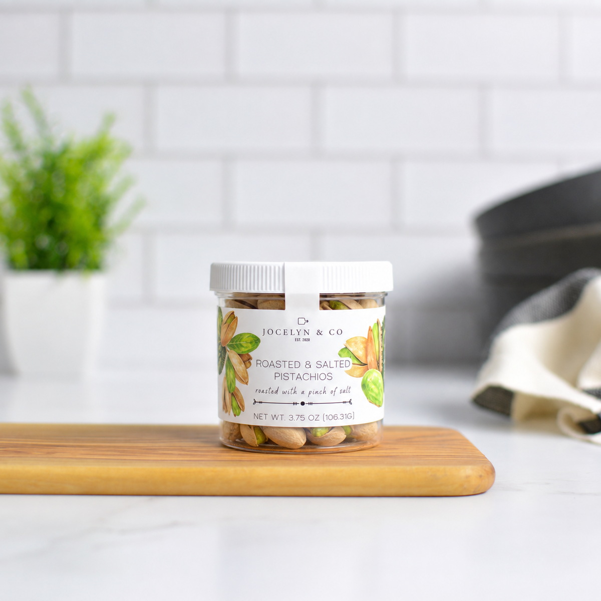 Jocelyn & Co. Roasted Pistachios Jar, upright on a wooden board in a softly lit kitchen setting